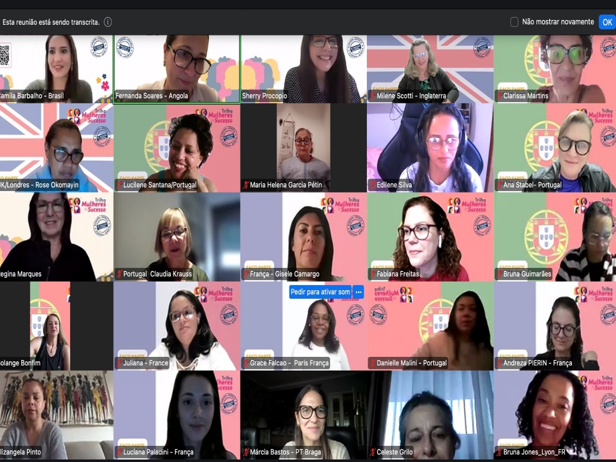 Captura de tela de uma videoconferência exibindo uma grade com 25 participantes, majoritariamente mulheres. Muitas utilizam fundos virtuais personalizados com bandeiras da Inglaterra, França, Portugal e o logotipo 'Trilha Mulheres de Sucesso'. Cada miniatura de vídeo apresenta o nome da participante e sua respectiva localização ou núcleo na parte inferior.