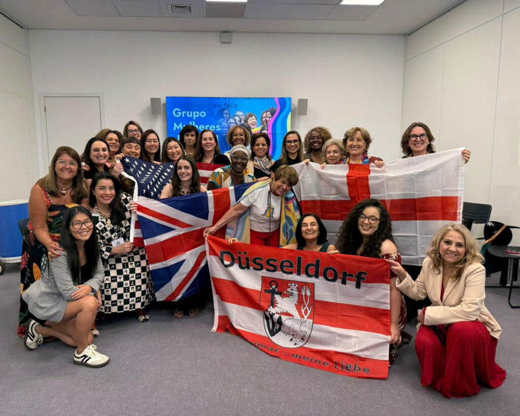 Grupo de mulheres reunidas em uma sala segurando bandeiras de diferentes países para uma foto coletiva.